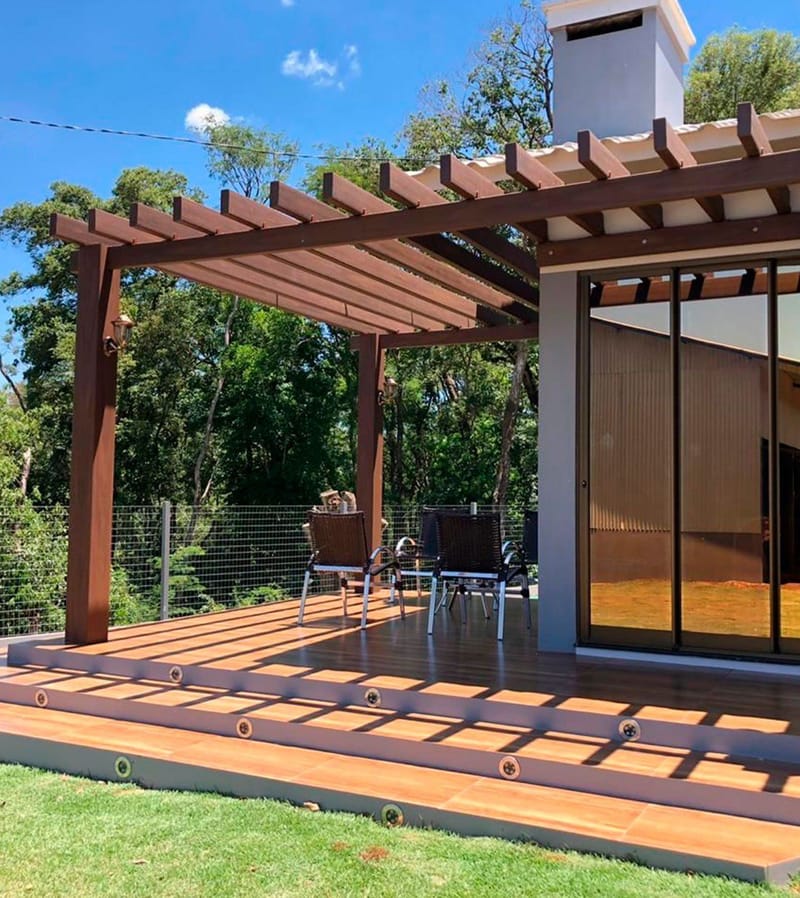 Área gourmet ao ar livre com mesa e cadeiras sob pergolado Linha Prime em madeira ecológica